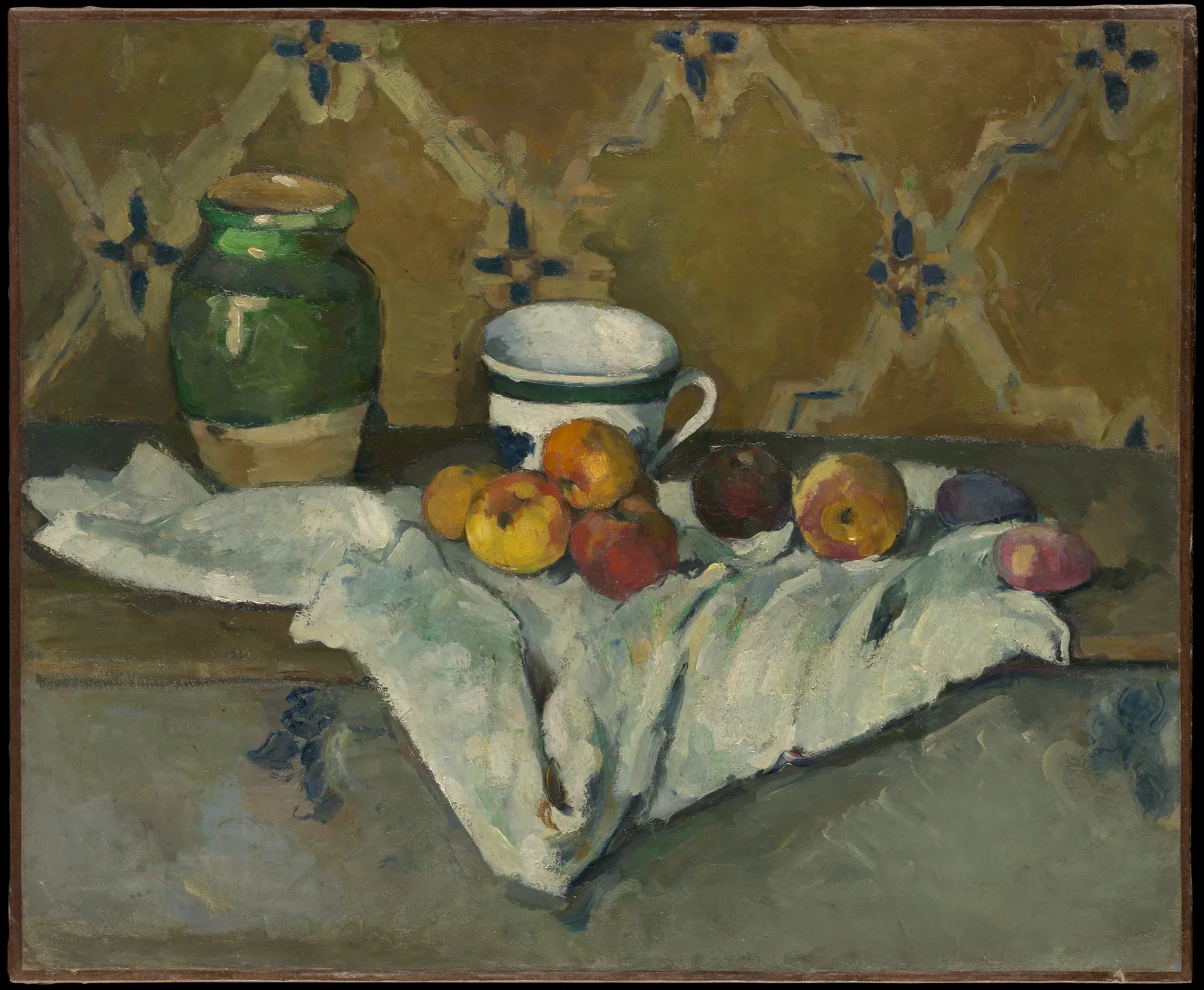 Paul Cézanne, Still Life with Jar, Cup, and Apples: ochre wallpaper with blue flower motifs and white diagonals forming a diamond pattern; in front, on a white napkin on a support, a green jar, a white cup with a green band, red and yellow apples and two purple and pink fruits. The front edge of the support crosses the picture.