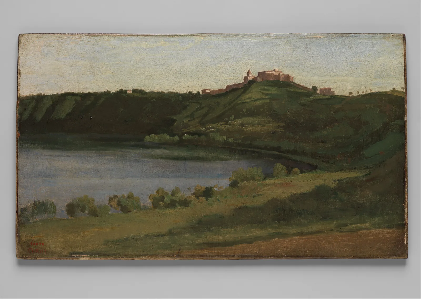 Camille Corot, Lake Albano and Castel Gandolfo: under a pale sky, pinkish buildings and a small dome stand on a green ridge; a blue-grey lake lies at lower left, with round bushes and grass in front. The edge of the wooden panel shows against a grey background.