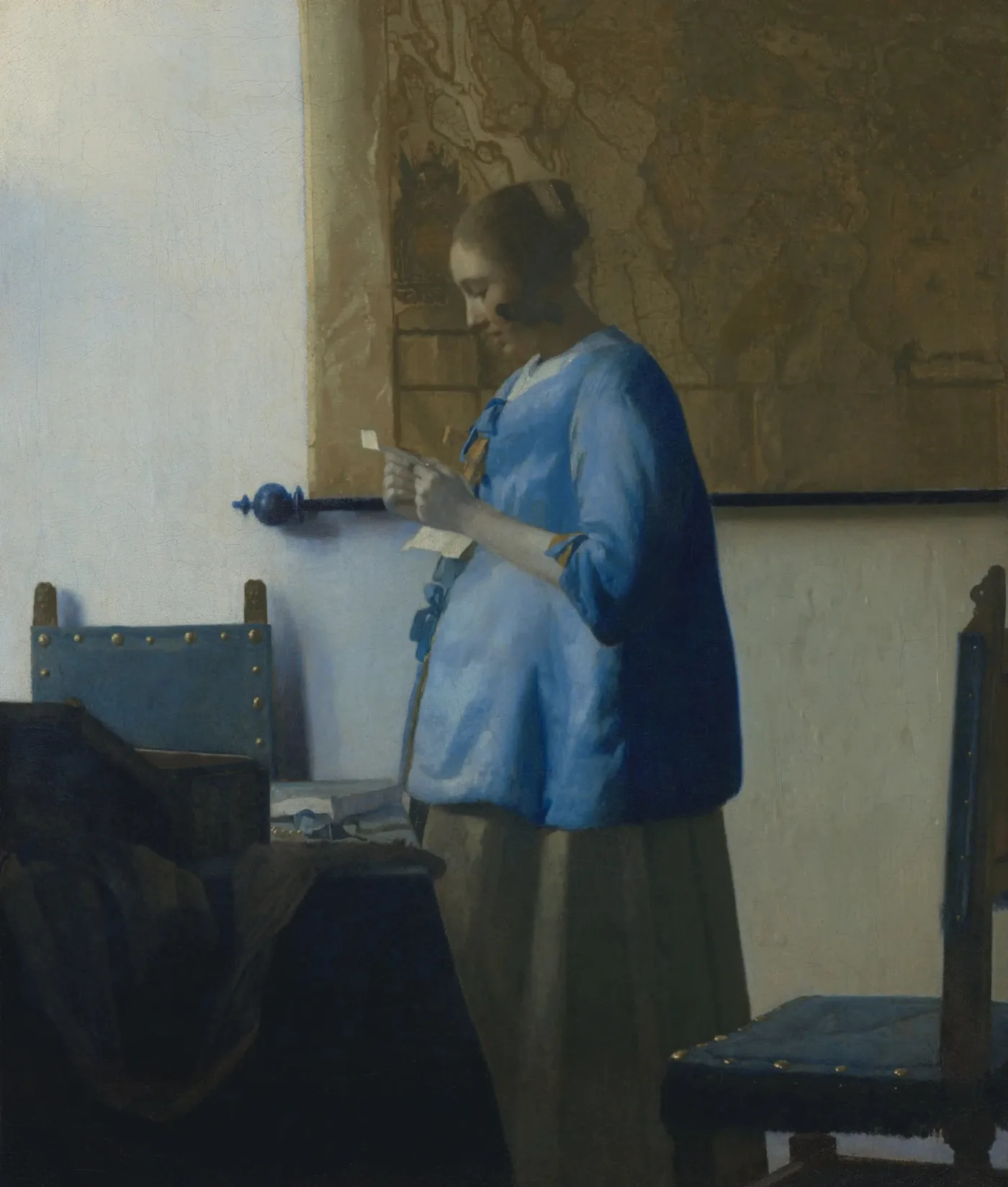 Johannes Vermeer, Woman in Blue Reading a Letter: a woman reading a letter, a large map behind her, and a table covered with a blue cloth. No window frame is visible in this photograph.