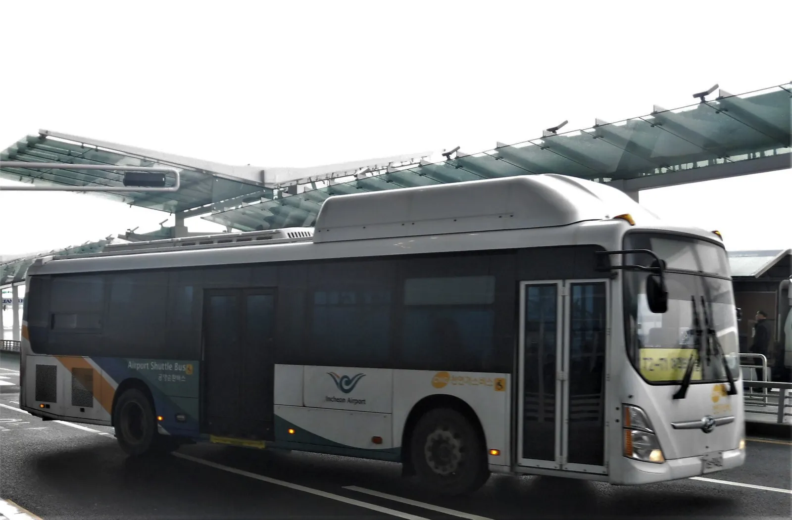 터미널 앞 도로에 선 흰색 인천공항 셔틀버스. 차체에 Airport Shuttle Bus 문구가 있다.